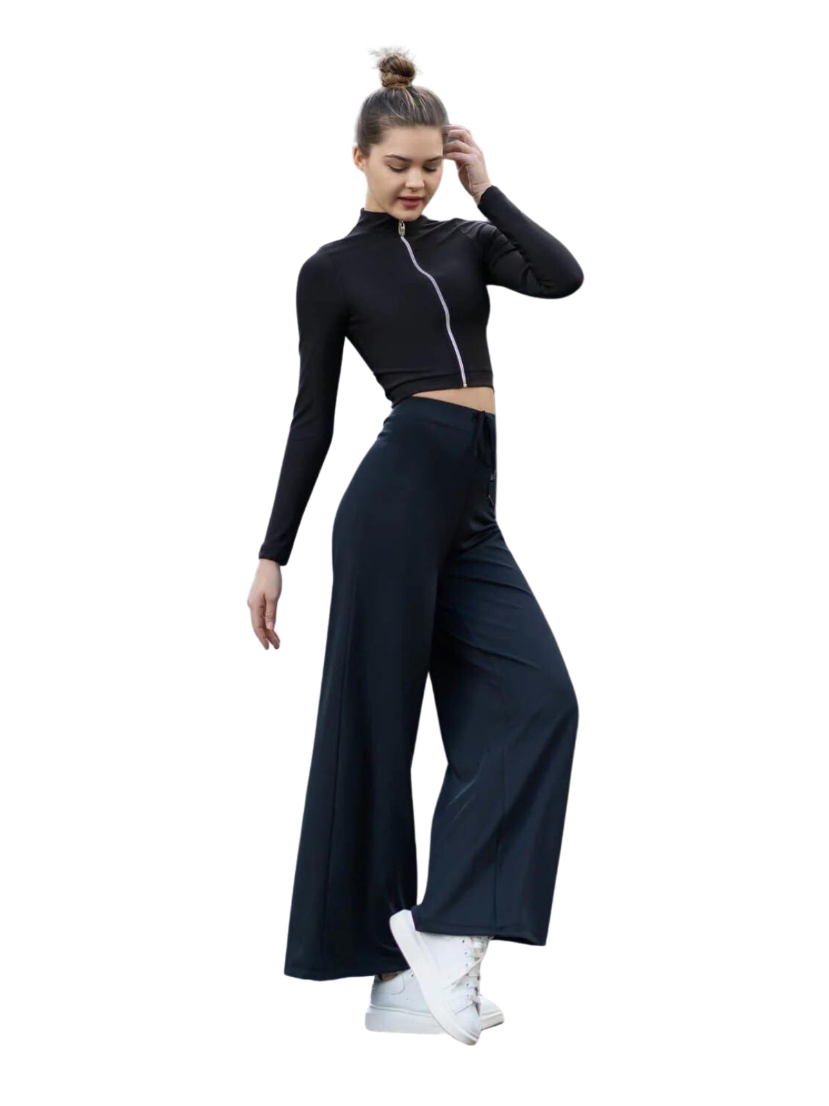 Frau in Lisminas 359 Mumbai Yoga Hose in Schwarz und mit weißen Turnschuhen steht vor einem weißen Hintergrund.